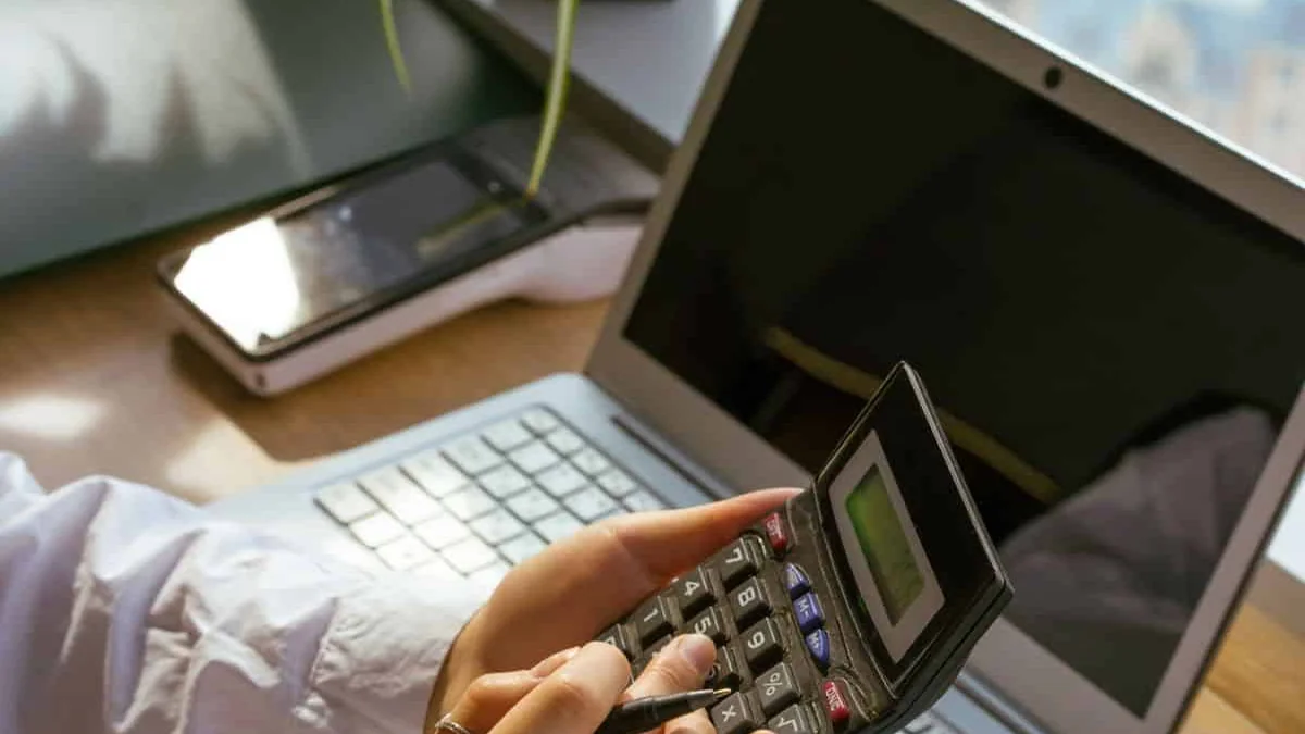Person using a calculator beside a laptop and notebook to plan a budget