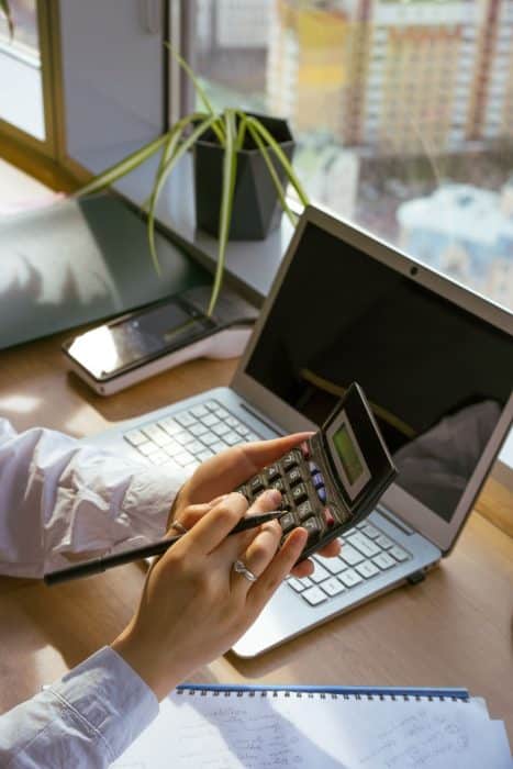 Person using a calculator beside a laptop and notebook to plan a budget