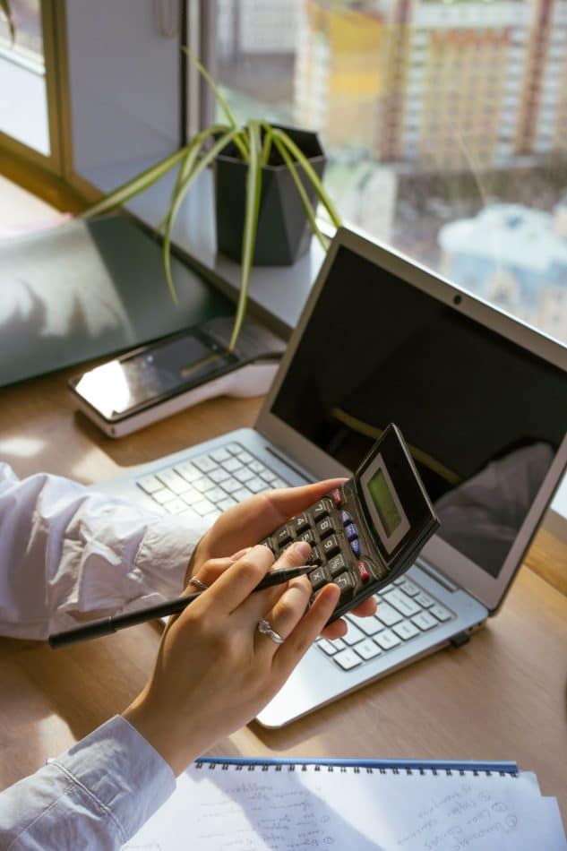 Person using a calculator beside a laptop and notebook to plan a budget
